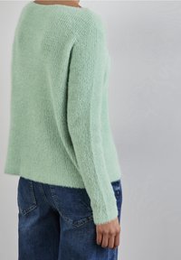 Mint green knit sweater showing a textured surface, long sleeves, and a relaxed fit. Paired with dark blue denim jeans.