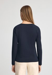 Marineblaue Langarmbluse mit Rundhalsausschnitt und figurbetontem Schnitt. Glatte Textur und minimalistisches Design. Kombiniert mit hellen Hosen.