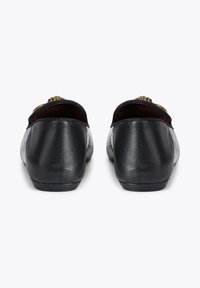 Chaussures en cuir noir avec des dos arrondis, présentant une texture lisse et un petit accent doré sur le dessus. Présentées en vue arrière.