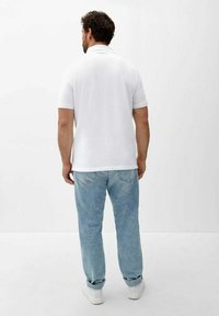 Polo shirt blanc à manches courtes avec un col classique, associé à un jean bleu clair et des chaussures blanches, vu de dos.