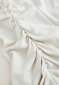 Tissu de couleur crème avec une texture douce et extensible, présentant des plis froncés et un léger côtelé, créant une apparence fluide.