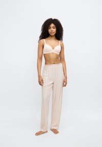 Reggiseno beige a scollo profondo con spalline sottili abbinato a pantaloni crema a righe verticali, di taglio ampio. Tessuto morbido con una texture liscia.