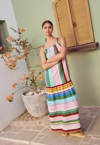 Striped maxi dress features multicolored vertical stripes in pink, green, yellow, and blue, with shoulder ties and a ruffled hem.