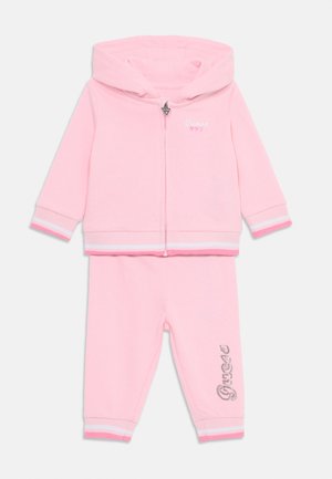 Rosa Kleinkinder-Jogginganzug mit einer zipfelkapuzenjacke mit Logo und passenden Hosen mit gestreiften Bündchen und Verzierungen.