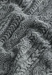 Tissu gris tricoté avec des motifs texturés en torsades et zigzags, montrant des plis et des détails de fil épais et doux.