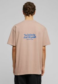 Short-sleeve, oversized t-shirt in light pink cotton. Features blue text reading "To Infinity And Beyond" on the back.