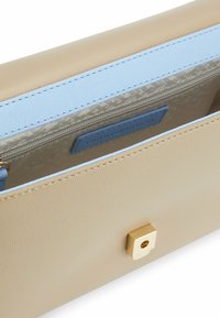 Beige læderpung med en guldfarvet firkantet lås, der har en lys blå indvendig foring, teksturerede mønstre og et lille blåt mærke indeni.