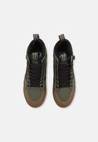 Zelené vysoké tenisky s texturovaným povrchem, černými tkaničkami a hnědými gumovými podrážkami. Obsahují kontrastní šedé pruhy na horních smyčkách.