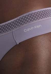 Ljust lila Calvin Klein-tanga med en texturerad midjeband med ett bikupemönster. Sömlös konstruktion och mjukt, elastiskt tyg.