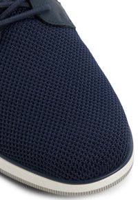 Granatowe siateczkowe sneakersy z teksturowaną cholewką, zaokrąglonym noskiem i kontrastującą białą podeszwą. Posiada tonalne sznurówki oraz gładki skórzany akcent.