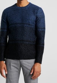 Pull col rond tricoté en dégradé de bleu à noir. Caractérisé par un tissu texturé ainsi que des poignets et une bordure côtelés.