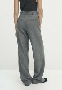 Pantalons à jambes larges gris, fabriqués en tissu texturé. Présentent une taille haute, des poches arrière et une finition lisse. Pas de motifs ou d'ornements visibles.