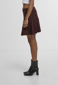 Bourgogne-ribbad minikjol med en utsvängd design och åtsittande midja, kombinerad med svarta ankelstövlar med en slät och glänsande yta.