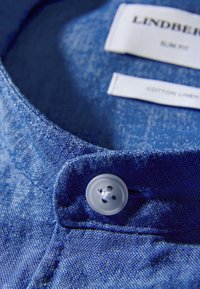 Colletto di camicia in cotone-lino azzurro chiaro con una finitura testurizzata, caratterizzato da un bottone bianco con design a quattro fori e etichette con marchio.