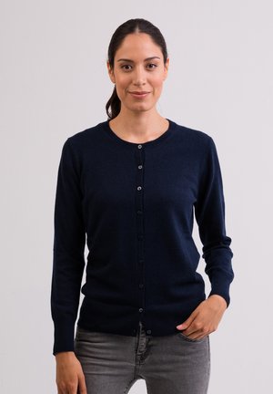 Gilet en tricot bleu marine à manches longues, col rond et fermeture à boutons. Texture douce avec une coupe ajustée. Boutons proéminents à l'avant.