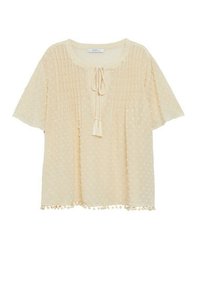 Light beige short-sleeve blouse with textured polka dots, vertical pleats on front, tassel tie at neckline, and pom-pom trim at hem.