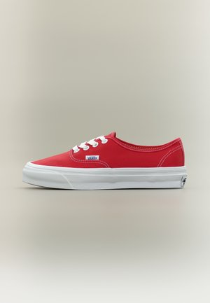 Baskets Vans basses rouges avec lacets blancs, semelle en caoutchouc blanche et logo Vans sur le côté et le talon, présentées sur fond neutre.