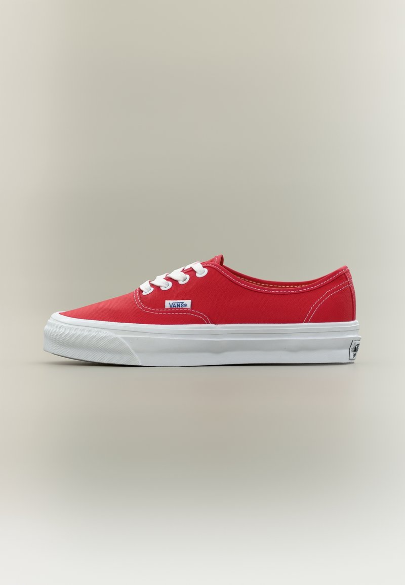 Baskets Vans basses rouges avec lacets blancs, semelle en caoutchouc blanche et logo Vans sur le côté et le talon, présentées sur fond neutre.