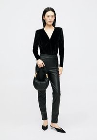 Body din catifea neagră cu decolteu în V, asortat cu pantaloni negri din piele ecologică, cu talie înaltă. Accesorizat cu o geantă neagră și tocuri ascuțite.