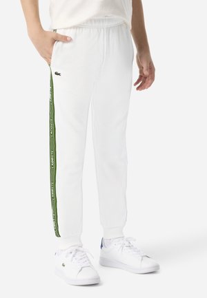 Hvite joggebukser med grønne striper på siden og "LACOSTE"-logo, elastisk midjebånd og mansjetter. Kombiner med hvite joggesko.