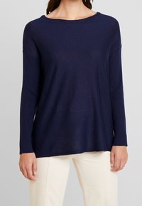 Granatowy sweter dzianinowy o luźnym kroju, szerokim dekolcie i prążkowanych rękawach; charakteryzuje się gładką fakturą i subtelnym układaniem.