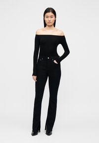 Haut noir à manches longues et épaules dénudées, associé à un jean noir taille haute évasé avec des fentes latérales. Texture lisse, design simple.