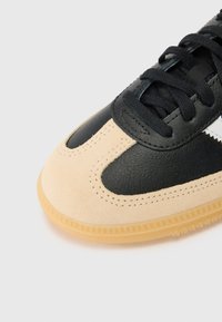 Sneaker med ovandel i svart läder, beige mocka på tåspetsen och kontrasterande sömmar. Platta svarta snören och en sula i gummigummi.
