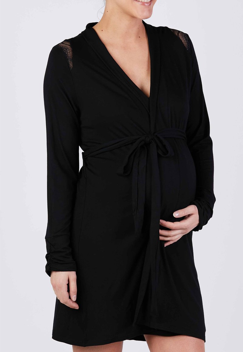 Robe de nuit noire en tissu doux, avec des manches longues, un décolleté en V profond et des accents en dentelle sur les épaules. Liée à la taille.