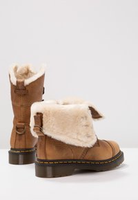 Paire de bottines en cuir marron avec doublure en fausse fourrure crème pliée, semelles noires et coutures jaunes.