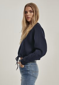Felpa cropped blu navy con tasca frontale e cordino. Abbinata a jeans aderenti azzurri con tasche posteriori e un lavaggio scuro.
