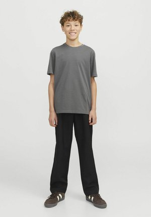 Grijze katoenen t-shirt met korte mouwen, gecombineerd met zwarte wijde broek en bruine sneakers met witte strepen.