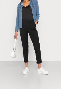 Pantaloni neri con risvolti, un top nero con pizzo e una camicia di denim blu. Scarpe da ginnastica bianche e una piccola borsa bianca completano l'outfit.
