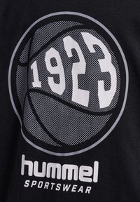 Svart T-shirt med en stor, cirkulär basketgrafik i grått med året "1923" och "hummel SPORTSWEAR" i fet vit text.