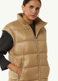 Beige Puffer-Weste mit hohem Kragen, Reißverschluss vorne und Seitentaschen. Verfügt über eine glatte, glänzende Textur und ein gestepptes Design.