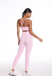 Svetlo roza športni modrček s križanimi naramnicami, v kombinaciji z visokimi svetlo roza leginami. Tkanina se zdi gladka in raztegljiva.