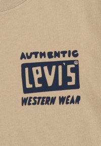 Tela de algodón beige con un texto en negrita de color azul marino que dice "AUTHENTIC LEVI'S WESTERN WEAR". Textura suave con un diseño clásico y casual.
