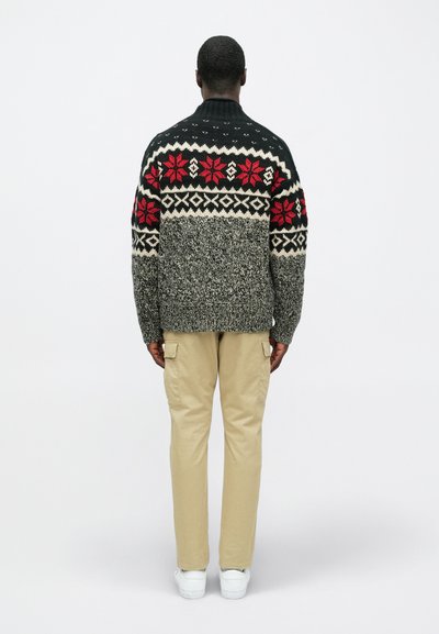 Pleteni pulover u crnoj, sivoj i krem boji s crvenim cvjetnim uzorcima. Uparite s bež cargo hlačama i bijelim cipelama za slojeviti izgled.