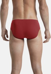 Slip da bagno rossi con una superficie liscia, caratterizzati da un design aderente e gambe alte, che mostrano una finitura opaca e una vita elastica.