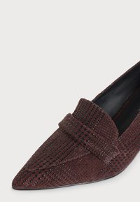 Mocassin en cuir tressé rouge foncé à bout pointu, avec une bride sur le dessus et une doublure intérieure noire.