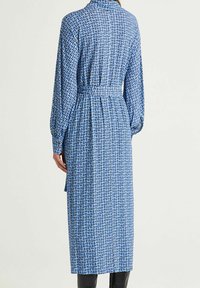 Vestito blu con motivo geometrico, maniche lunghe, vita cinchata e orlo al ginocchio. Il materiale sembra leggero e con una texture.