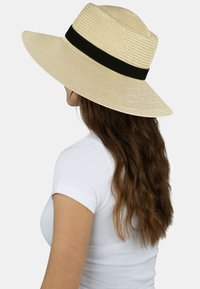 Beiger Strohhut mit breiter Krempe und schwarzem Band. Verfügt über eine strukturierte Oberfläche und eine runde Krone. Geeignet zum Schutz vor Sonne.