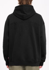 Zwarte hoodie met complexe zwarte borduursels op de achterkant die een bergketen afgebeeld. Gemaakt van zachte, gestructureerde stof.