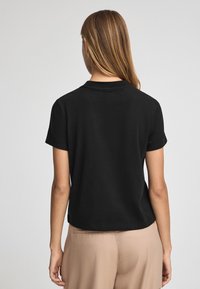 Camiseta negra de manga corta hecha de algodón con cuello redondo y un corte relajado, combinada con pantalones beige. Textura suave.