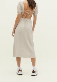 Beiges Kleid mit Puffärmeln, offenem Rücken und Lacing in Kreuzform, mit einem mittellangen Design. Getragen mit weißen Sneakern und gemusterten Socken.