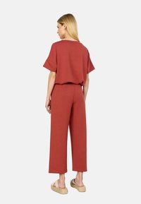 Rust-colored two-piece outfit featuring a loose-fitting top with short sleeves and wide-leg pants, made from soft fabric with a smooth texture.