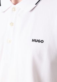 Polo bianco a maniche corte, con colletto classico e tre bottoni. Logo "HUGO" in nero sul lato sinistro.