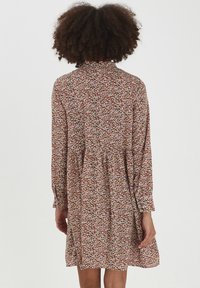 Abito a maniche lunghe con un motivo floreale in rosso, rosa, bianco e verde. Presenta un colletto e scende delicatamente dai fianchi. Tessuto strutturato.