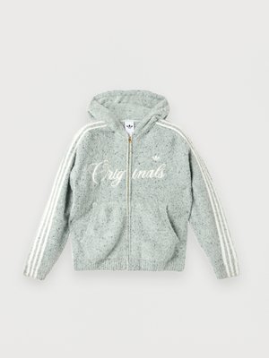 Ung mann iført en lys grå, myk hettegenser med glidelås, hvite striper på ermene og hvit skrift, kombinert med svarte bukser.