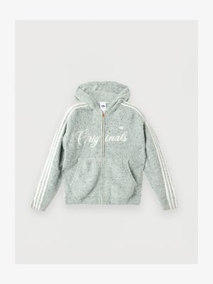 Jeune homme portant un sweat à capuche zippé gris clair en tissu pelucheux avec des rayures blanches sur les manches et un texte blanc en écriture, assorti à un pantalon noir.