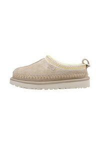 Chaussure en suède beige à enfiler avec une épaisse semelle beige, un bord cousu jaune et blanc, et une languette au talon.